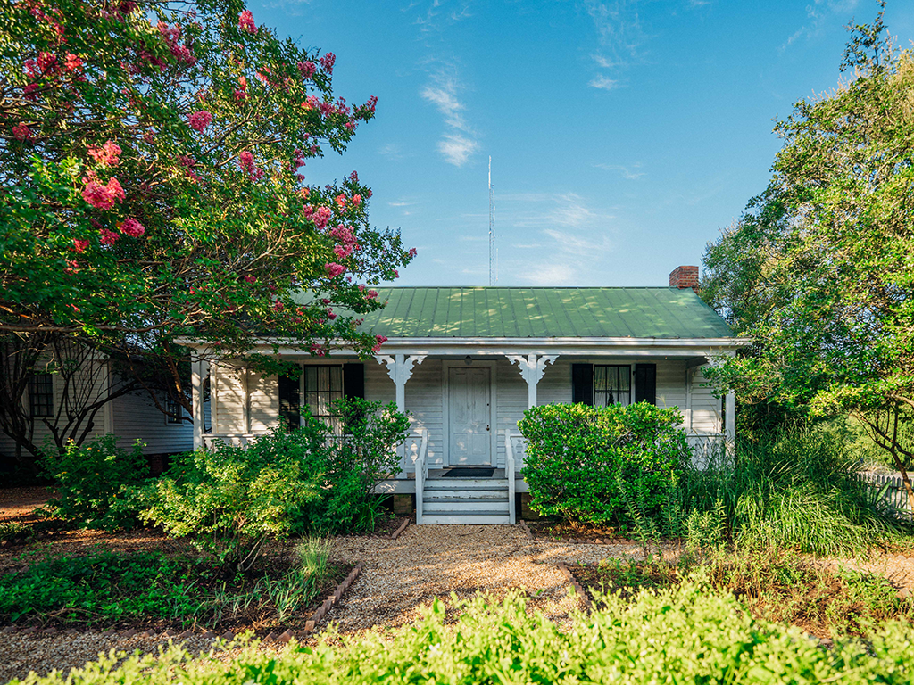 a photo of Rose Cottage, a small white cottage with a green roof